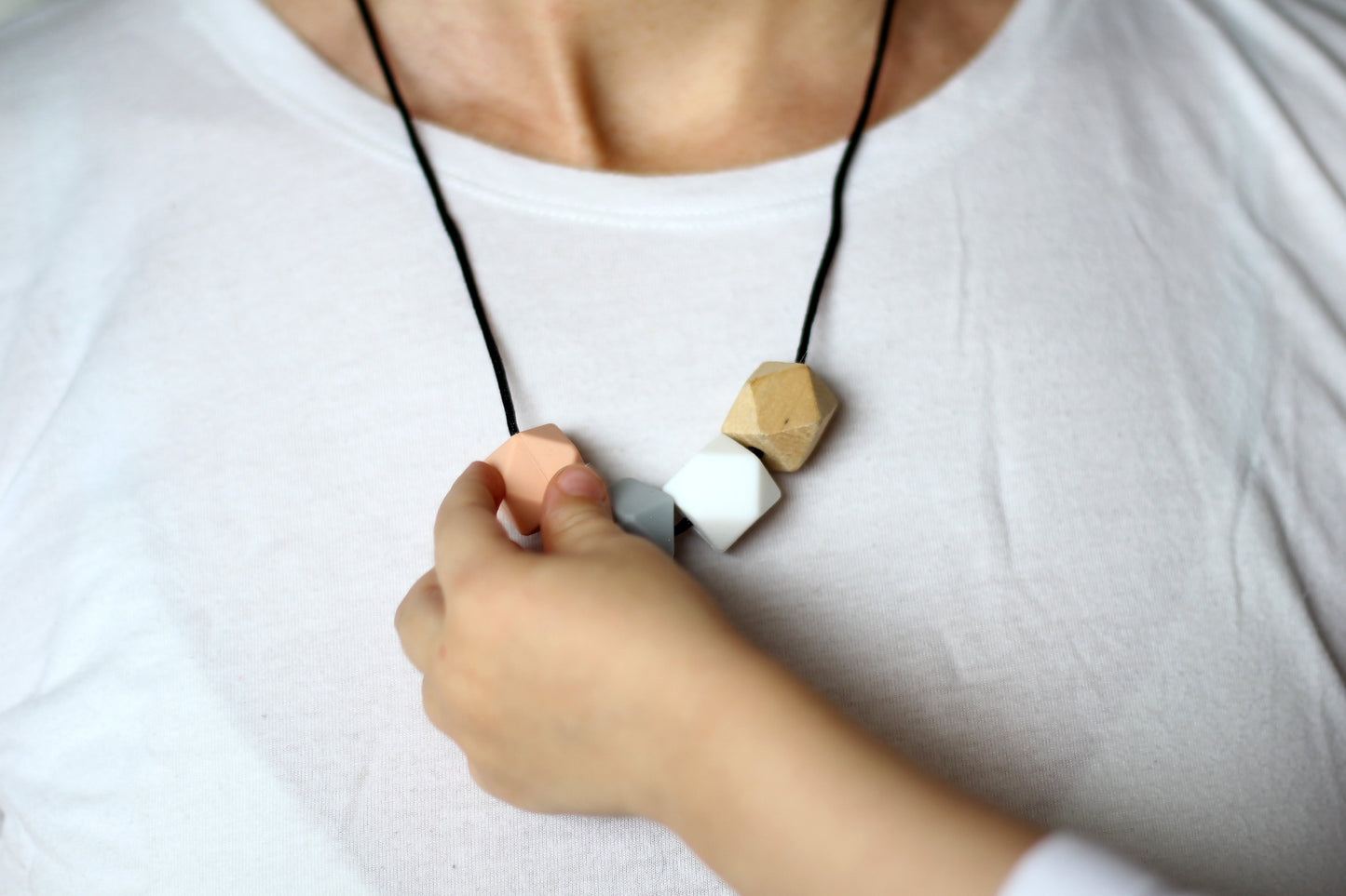 Little baby hand fiddling with Peach Teething Activity Necklace natural wood & silicone!